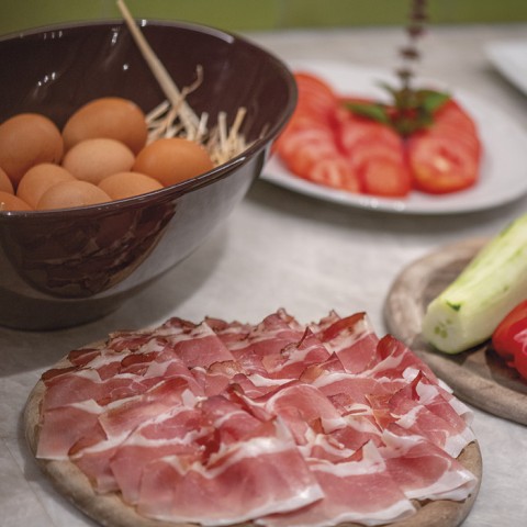 L'immagine mostra il buffet della colazione. Sono visibili uova appena cotte, pancetta, pomodori e cetrioli.