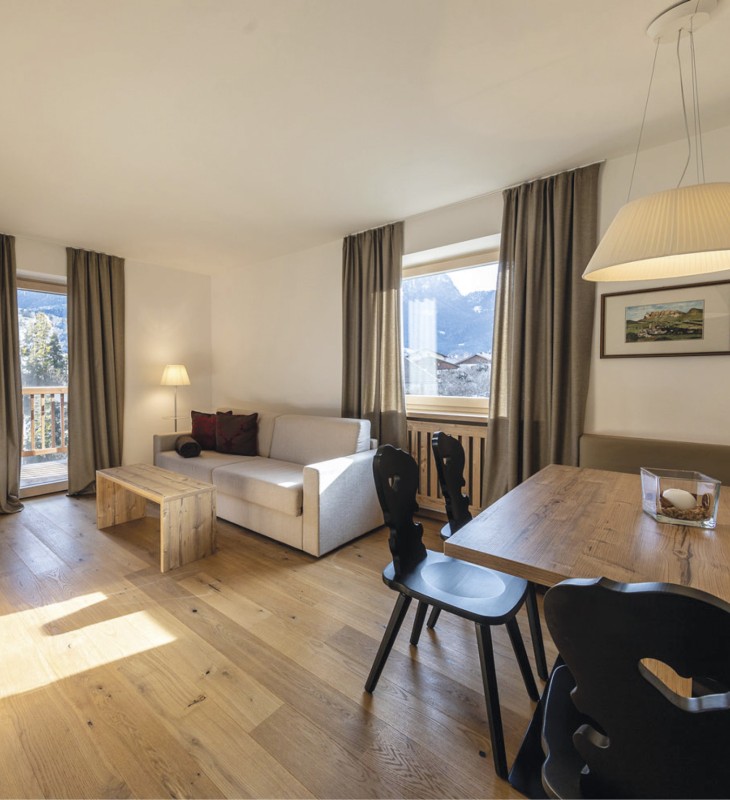hubertus dolomites a fiè allo sciliar | Il tuo rifugio alpino in Alto Adige. L'immagine mostra la zona giorno dell'appartamento. Si vede un divano, il tavolo da pranzo e il balcone.