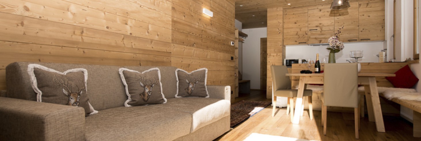 Accogliente divano sotto profumati rivestimenti in vero legno in uno chalet rustico e romantico per vacanze nella natura, direttamente sull'Alpe di Siusi.