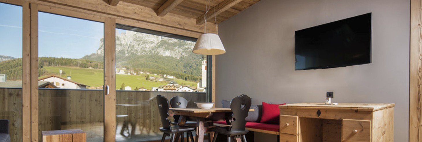 hubertus dolomites a Fiè allo Sciliar | abitare in modo accogliente ai piedi dello Sciliar. Il soggiorno di un appartamento con sedie nere e una televisione.