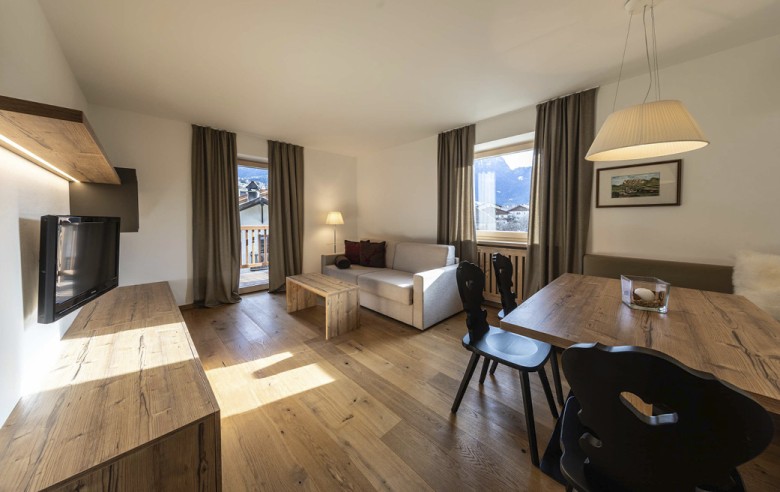 La zona giorno dell'appartamento. Si vedono la TV e il divano, così come il tavolo da pranzo con sedie nere.