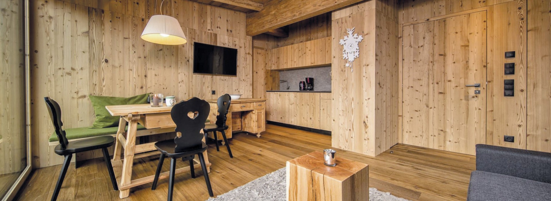 Il soggiorno di un appartamento per vacanze, dove si trova un tavolo di legno con sedie nere e la cucina sullo sfondo.