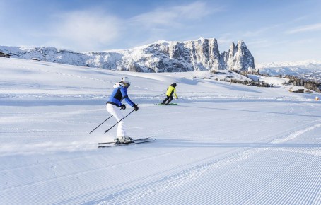 hubertus dolomites Fiè allo Sciliar | Magia invernale sull'Alpe di Siusi: la vostra porta d'accesso al comprensorio sciistico dei superlativi Il comprensorio sciistico dell'Alpe di Siusi e due sciatori e lo Sciliar sullo sfondo.