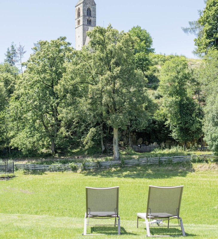Da due sdraio in giardino si possono vedere ampi prati verdi e la chiesa del paese.