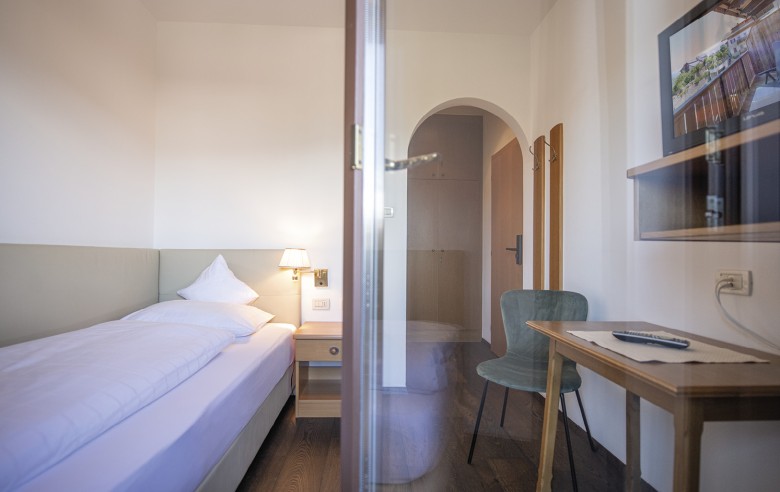 Un letto singolo con scrivania e televisore. La foto è stata scattata dal balcone.