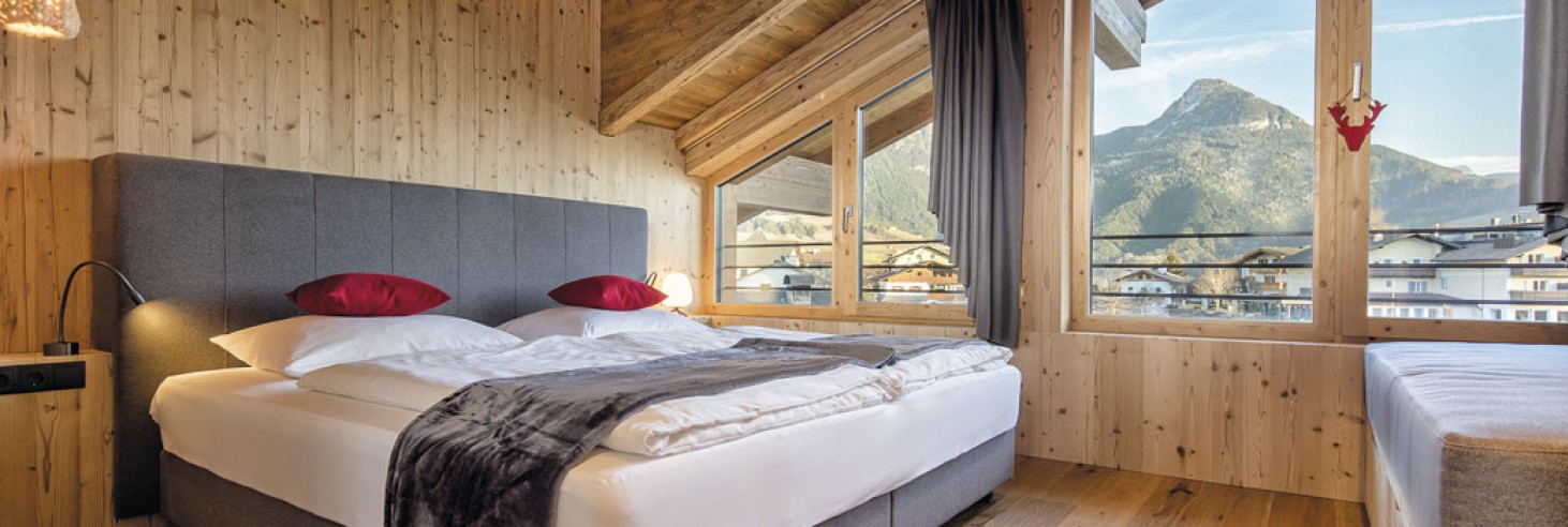 Hubertus Dolomites a Fiè allo Sciliar | Camere confortevoli per un soggiorno rilassante. Una stanza con un letto e cuscini rossi.