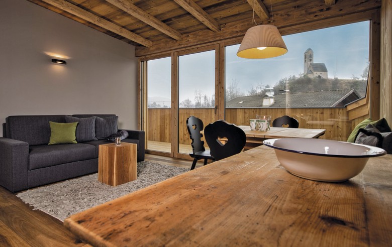 La zona giorno della camera. Si vedono un divano, un tavolo in legno con sedie nere e il balcone con vista.